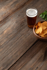 Glass of beer with bowl of chips on rustic wooden table, garnished with fresh parsley, creating cozy atmosphere