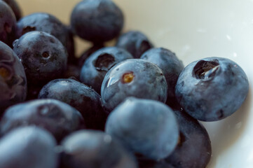 Bowl of blueberries is shown in a close up. The blueberries are fresh and plump, and they are arranged in a way that makes them look like they are ready to be eaten. The bowl is white