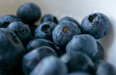 Bowl of blueberries with a few of them missing. The bowl is white. The blueberries are fresh and juicy