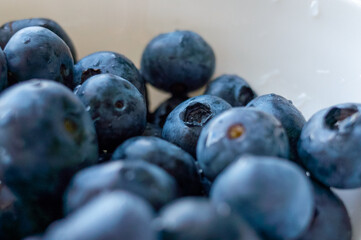 Bowl of blueberries with a few of them missing. The bowl is white. The blueberries are fresh and juicy