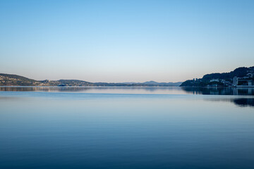 Serene lake at dawn with calm waters reflecting the clear sky over distant hills and a tranquil shoreline in the early morning light