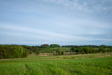 Obraz premium Wind turbine stands tall among green fields and forests in a rural landscape on a clear day