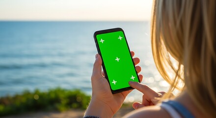 Woman holding smartphone with green screen mockup near the sea at sunset