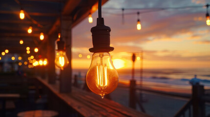 Beautiful sunset illuminates beachside setting, with glowing light bulbs hanging from wooden structure, creating warm and inviting atmosphere. ocean waves gently lap shore, enhancing serene