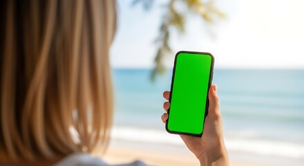 Woman holding a smartphone with a green screen on a sunny beach day