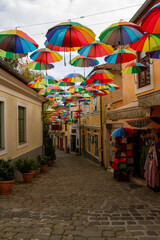Fototapeta premium Colorful Umbrella Installation Over Narrow Cobblestone Street 
