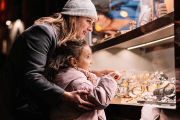 Mother and daughter admiring jewelry in a shop window at night