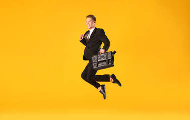 Businessman with briefcase jumping on orange background