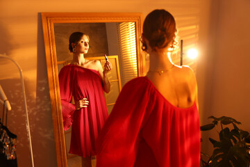 Beautiful woman applying lipstick while getting ready near mirror indoors