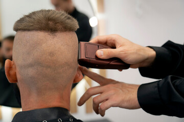 A man is getting a haircut at a barbershop. The barber is using clippers on the back of the man's head to cut his hair. The time of day appears to be daytime, due to the lighting