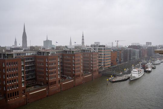 View of the historic warehouse district along the river in Hamburg on a foggy morning with ships docked along the waterfront - Powered by Adobe