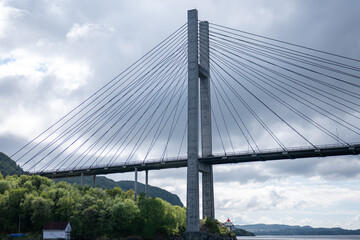 Suspension bridge spanning a river with green forests and cloudy skies in a serene landscape