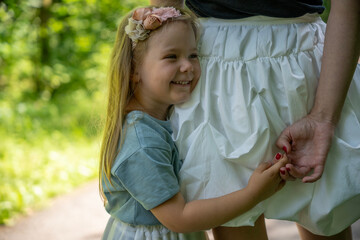 Low-angle shot of a happy child holding mother&rsquo;s hand and hugging her side at eye level, feeling safe with parent in a warm and loving moment outdoors.