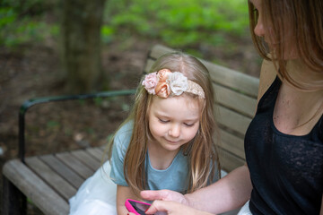 Fototapeta premium Outdoor portrait of a mother and child spending family time in a park, using a smartphone together, enjoying modern digital parenting and bonding in natural light.