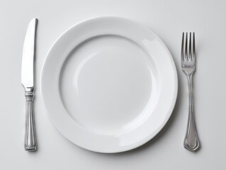 Overhead view of a minimalist place setting a clean white plate flanked by a knife and fork on a bright white surface
