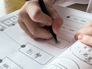 A young student sits at a wooden desk working on basic math exercises, steadily developing essential problem solving skills.