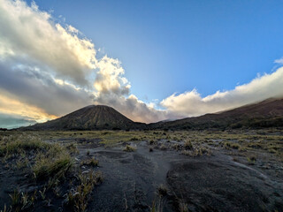 A dramatic wide-angle landscape plain under a bright blue sky with large, beautiful clouds. The scene is framed by two large hills or mountains on either side. 