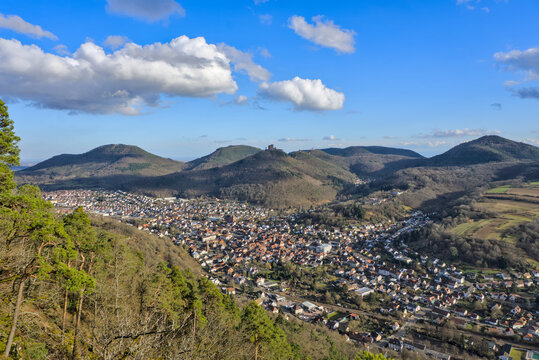 Annweiler am Trifels, Germany: An aerial view of the town of Annweiler am Trifels nestled in a valley, with the ruins of Trifels Castle visible on a forested hill in the background