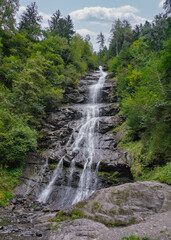Harter Schleierwasserfall: A view of the multi-tiered Harter Schleierwasserfall cascading down a rocky cliff face, surrounded by a lush green forest.

