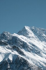 Snow-capped mountain peak under a clear blue sky, showcasing rugged textures and dramatic slopes of white and grey