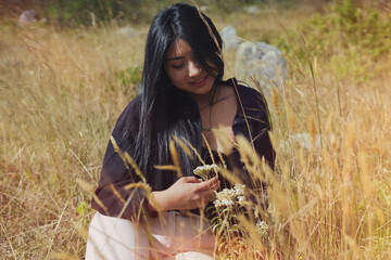 Young woman picking flowers in a field of dry grass