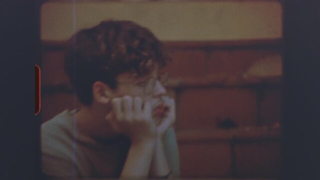 Teenage boy wearing glasses sitting on stairs in thoughtful pose on retro super 8mm vintage film