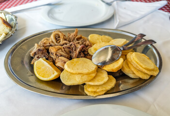 A gourmet appetizer of fried calamari and potatoes on a stainless steel platter, set on a restaurant table for a delicious meal