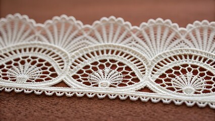 Beautiful white lace with a decorative pattern and scalloped border is elegantly displayed on a warm brown textile background.