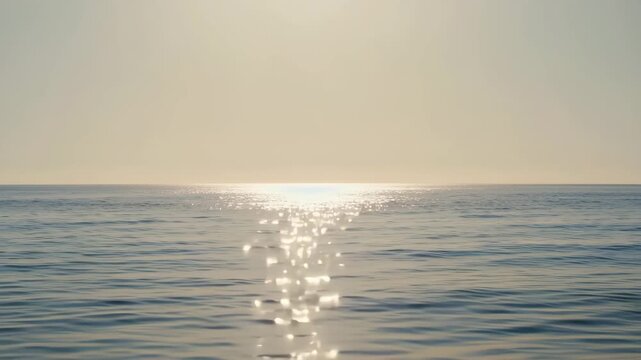 Golden sunlight glistening on the gentle waves of a calm ocean under a clear sky, creating a peaceful atmosphere.