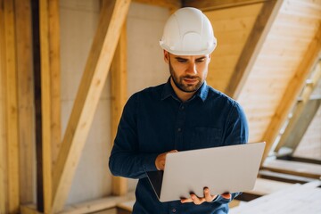 Construction Worker Using Laptop Inside Building Examining Plans and Overseeing the Project Management.