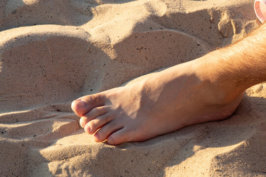 Male bare feet standing on wet sand of beach on sunny summer day in Ukraine