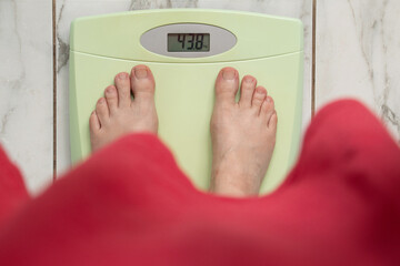 Female bare feet in red t-shirt on green electronic scales showing 43 and 8 kg on white tile