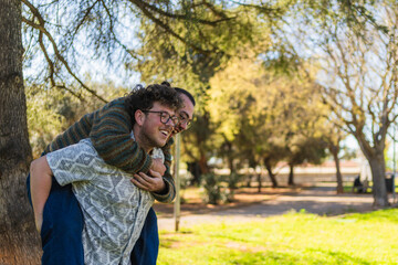 Two men enjoying a piggyback ride in a park, expressing their love and happiness