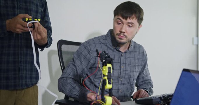 Closeup team adult male engineer collaborate on robotic hand project using AI code solutions machine learning at tech workspace. Artificial intelligence interface, collaboration prototype development.