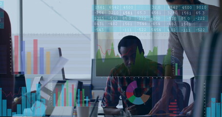 Pointing man in sweater guiding coworker in plaid at office desk with monitor, floating data charts