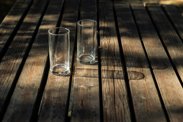 bicchieri di vetro, trasparenti e vuoti, su un tavolo di legno, illuminati dal sole, che proiettano le loro ombre lunghe sulla superficie