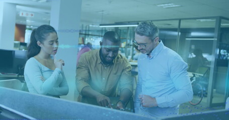 Pointing at digital display, three colleagues collaborating at modern office desks, with bicycle