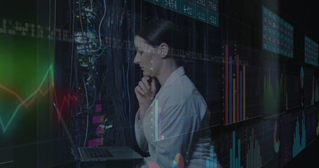 Analyzing woman in blazer reviewing financial charts in data center, with laptop and cables