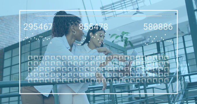 Collaborating women wearing white shirts at office atrium railing, using laptop with data overlay