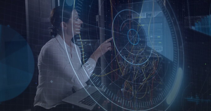 Kneeling technician pointing laptop at rack in server room monitoring holographic UI, copy space