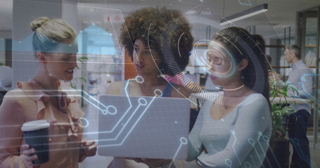 Discussing women collaborating around laptop in open-plan office, with coffee and digital overlay