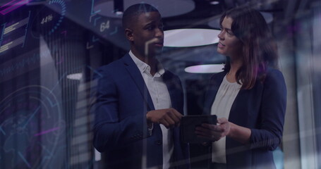 Collaborating professionals in suits analyzing data on tablet behind glass wall with digital charts