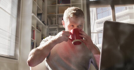 Sipping coffee man checking laptop screen at home office, with red mug, blinds and bookshelf