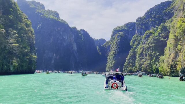 Tour boats in turquoise waters surrounded by towering limestone cliffs at Maya Bay, in Koh Phi Phi islands, Thailand under a bright sunny sky