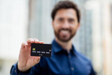 Handsome businessman holding a credit card outdoors with city buildings in blurred background