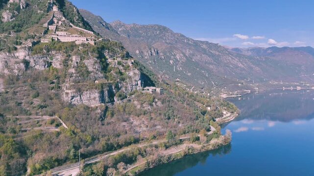 Aerial shot of Lake Idro in front of Rocca d'Anfo which is nestled on forested mountain with a road