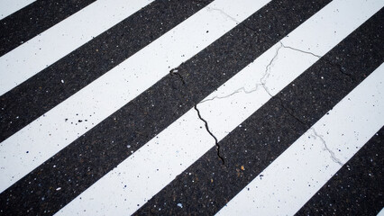 Fototapeta premium Cracked pavement crosswalk with white stripes, showcasing urban wear and tear. contrast between dark asphalt and bright lines creates striking