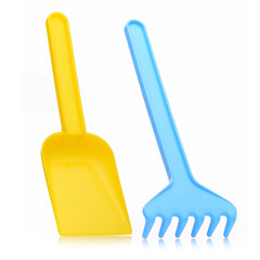 A yellow plastic shovel and a blue rake on a white background for children playing with sand and earth.