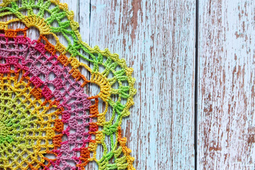 Top view photo of a bright multicolored crochet doily placed on rustic weathered wooden background. Perfect for craft blogs, handmade product catalogs, DIY design, and vintage-style backgrounds.