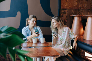 Modern women use mobile phones at a meeting while sitting in a cafe.